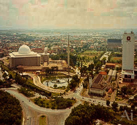 Aerial view of Istiqlal Mosque, its dome and minaret, with Pertamina Tower and surrounding streets in central Jakarta.